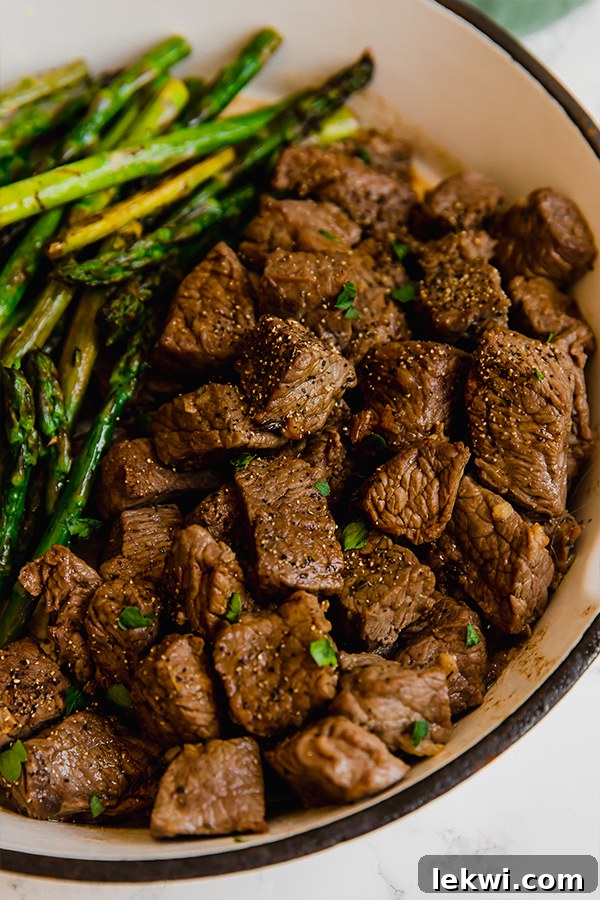 A sturdy cooking dish filled with succulent garlic balsamic steak bites and perfectly roasted asparagus, fresh out of the oven and ready to be enjoyed.