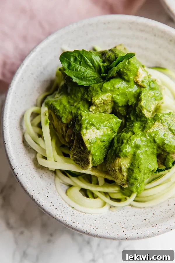 A white bowl with zoodles topped with slow cooker pesto chicken on it. Tender pesto-infused chicken breasts served over a bed of fresh zucchini noodles.
