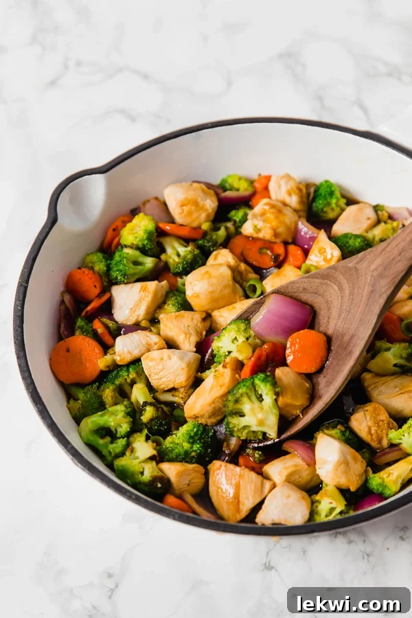 A white cooking dish filled with teriyaki chicken stir fry after cooking with a wooden spoon in it.