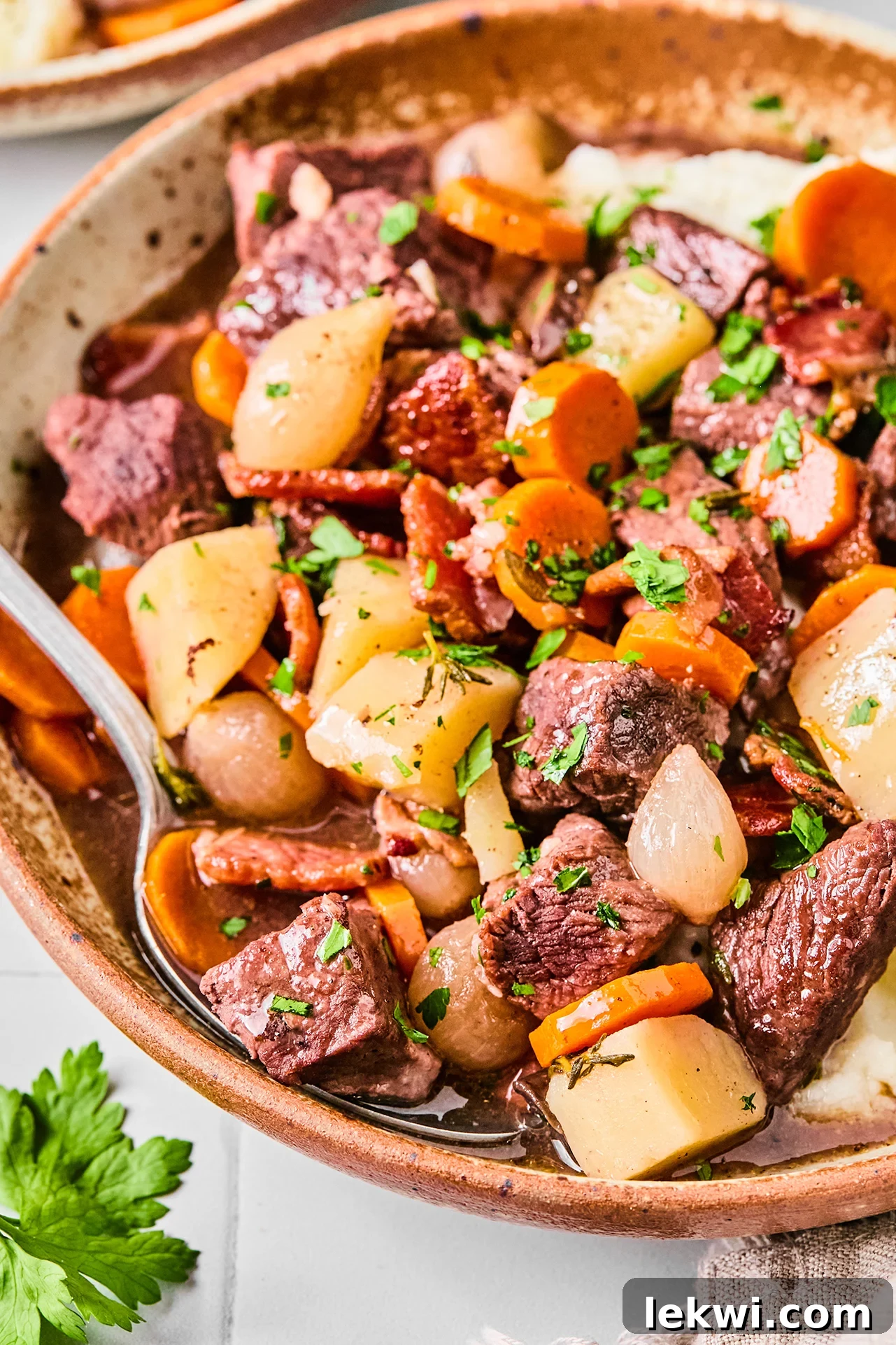 Slow cooker beef bourguignon in a large bowl with a spoon.
