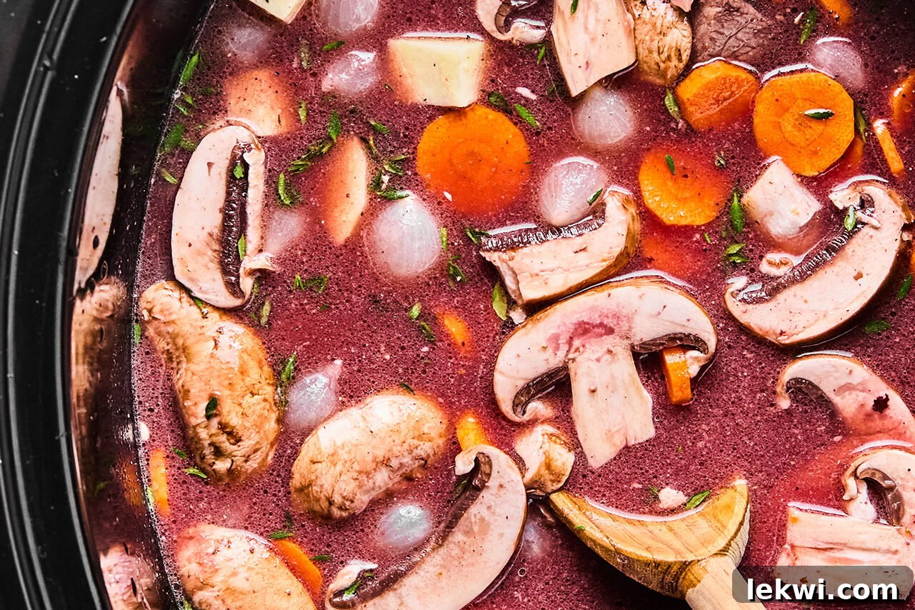A slow cooker filled with vegetables, broth, and wine before cooking.