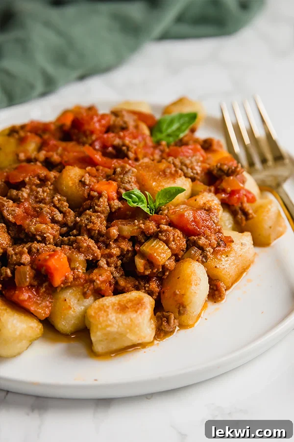 A white plate filled with gnocchi bolognese and a fork next to it.