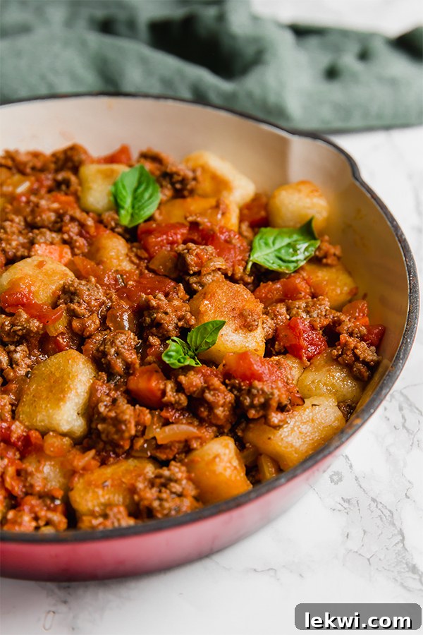 A serving dish filled with gnocchi bolognese and topped with fresh herbs.