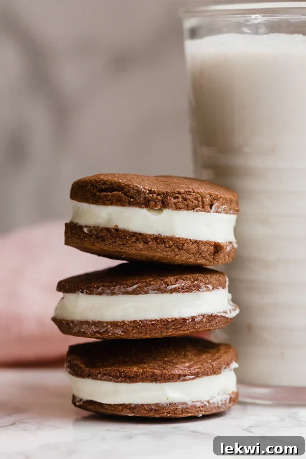 A stack of perfectly crafted homemade Paleo Oreo cookies, glistening with their creamy filling, sitting next to a glass of refreshing milk. The image evokes a sense of nostalgic comfort and deliciousness.