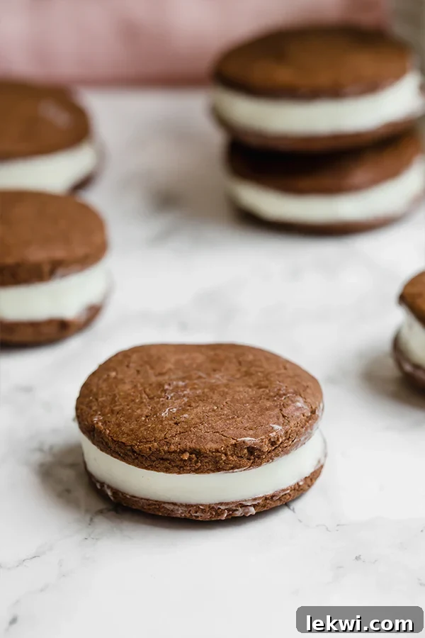 Two homemade Paleo Oreo cookies, one whole and one with a bite taken, showcasing the dark chocolatey cookie wafers and the luscious white cream filling.