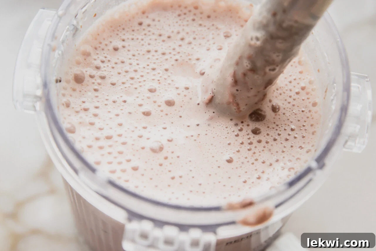 The pint container of a creami filled with all the ingredients and an immersion blender mixing it.