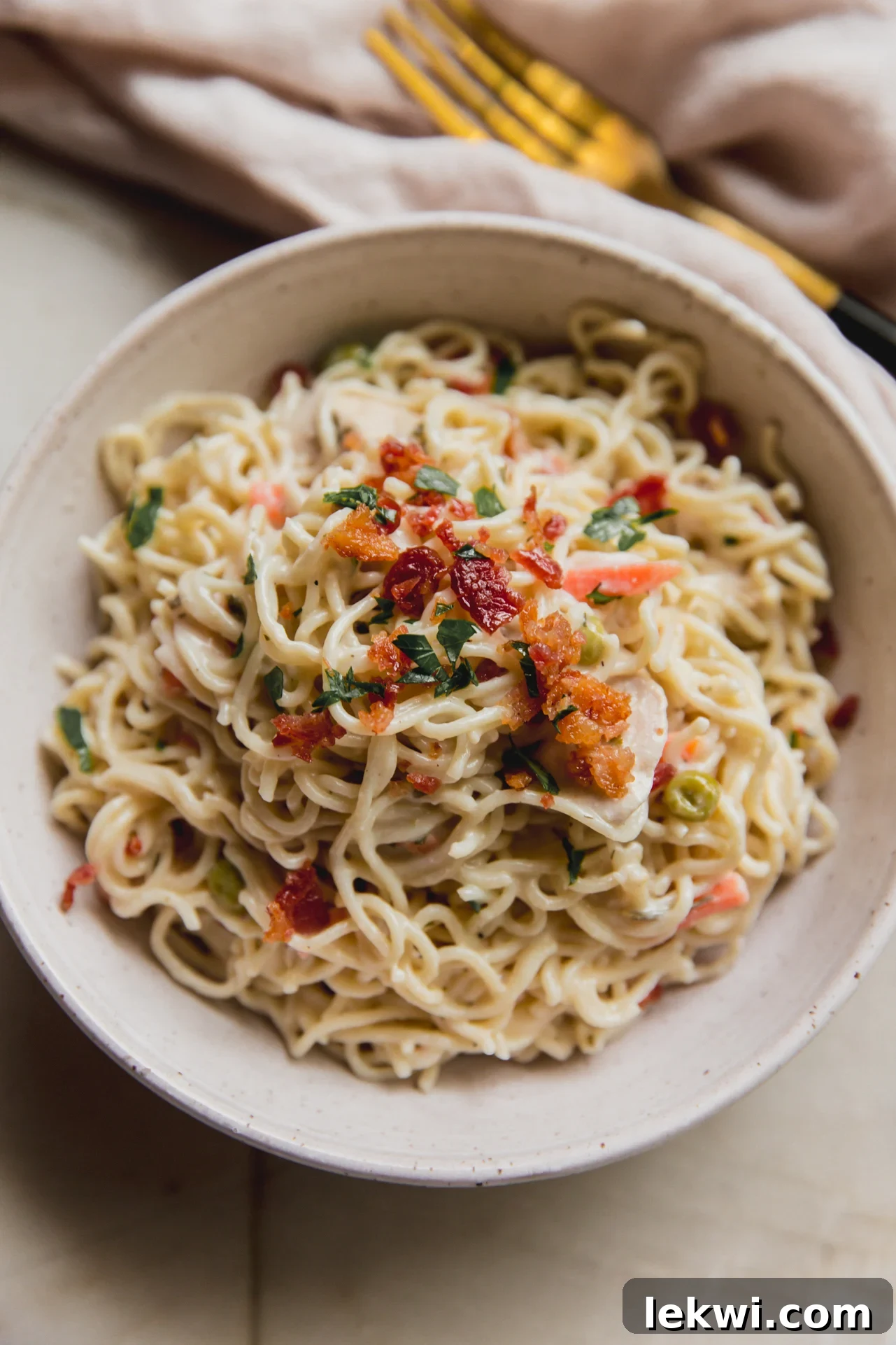 A serving of bacon ranch ramen bake in a bowl, generously topped with fresh parsley and crispy bacon bits, ready to be enjoyed.