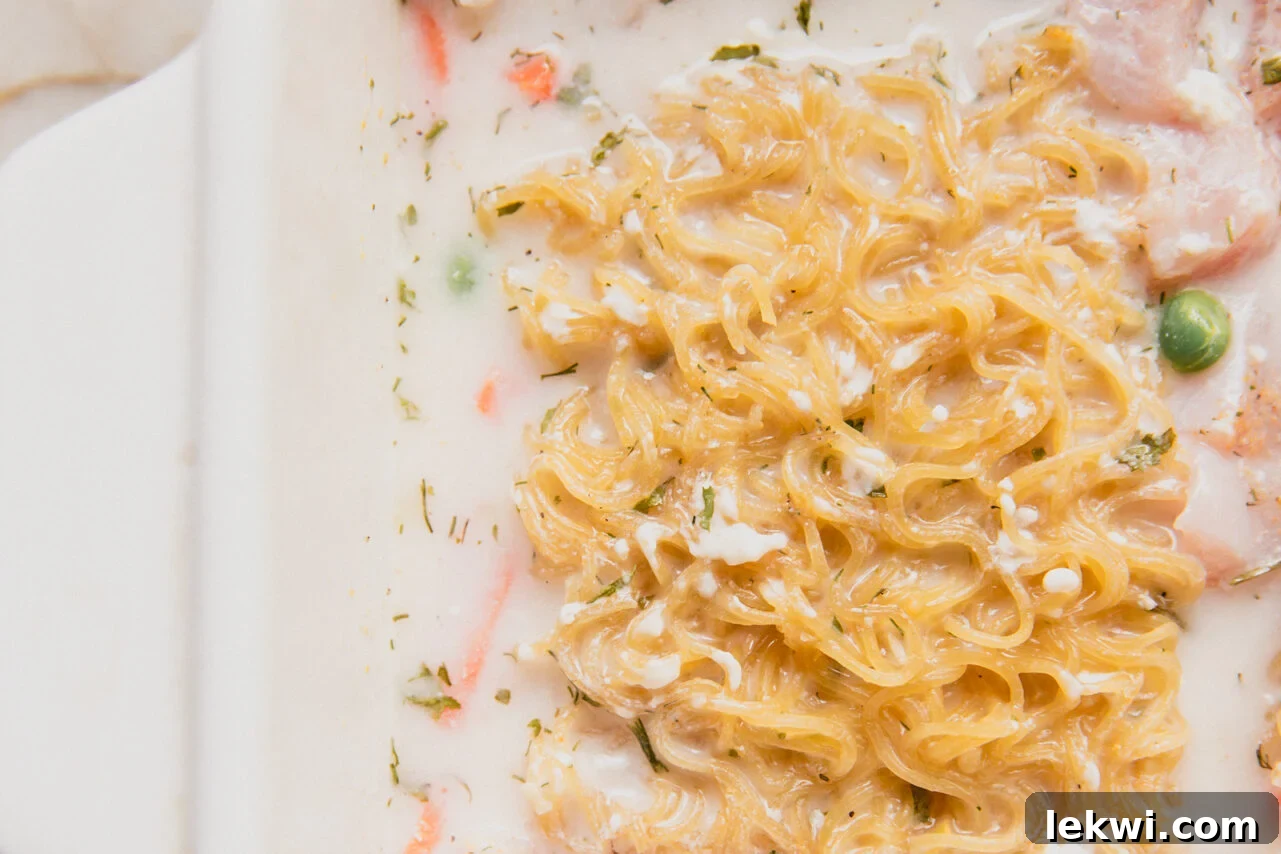 Coconut milk, lemon juice, and dairy-free cream cheese have been added to the ramen, chicken, and vegetables in the casserole dish.