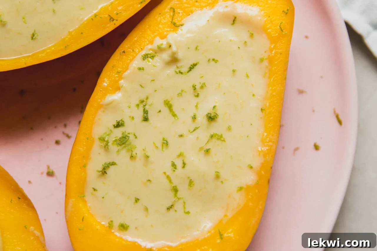 Tropical Mango Coconut Posset 7 Mango posset in a hollowed mango half, topped with lime zest, sitting on a pink plate.