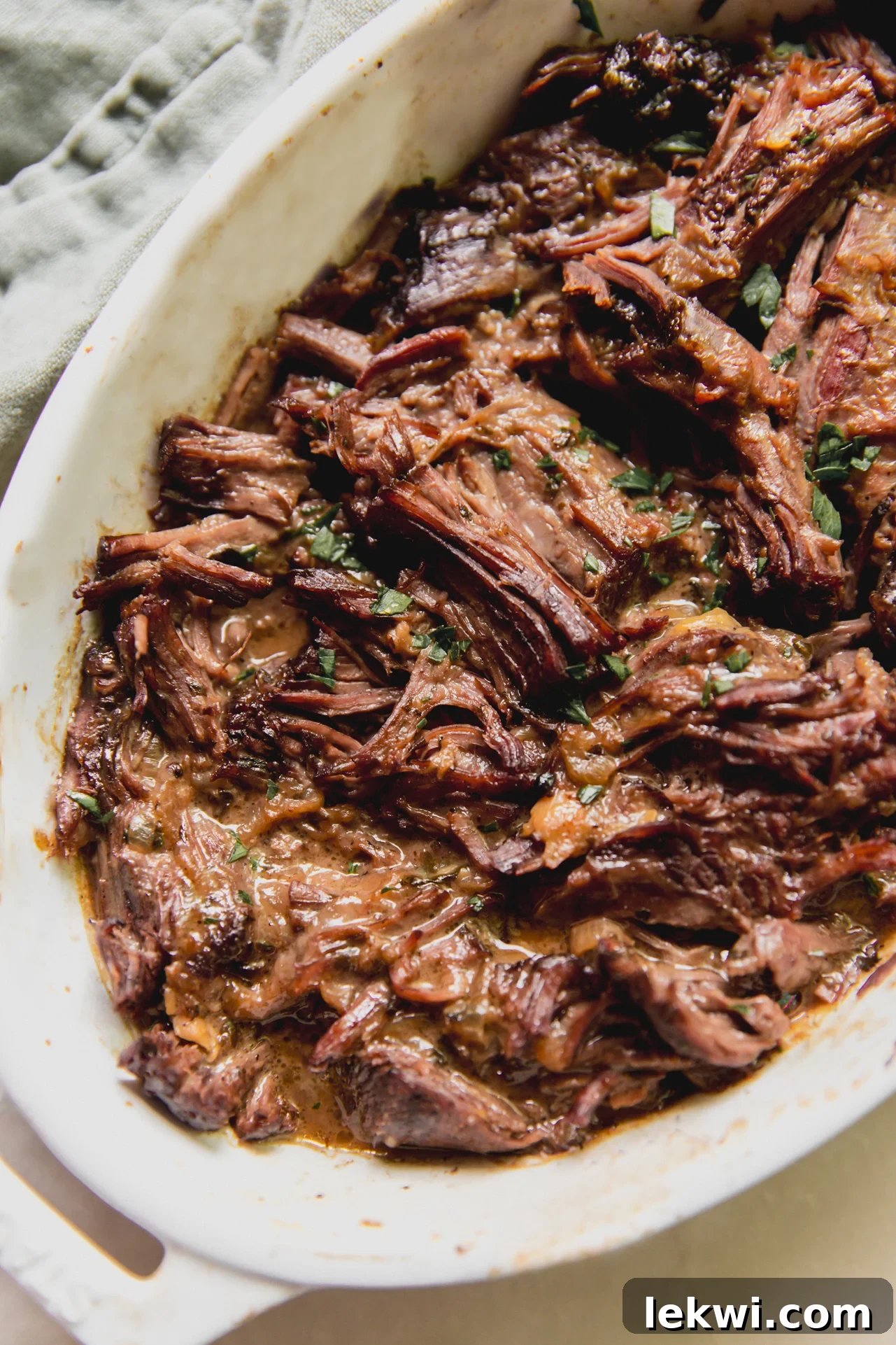 Shredded Mediterranean pot roast in a large white baking dish, ready to serve.