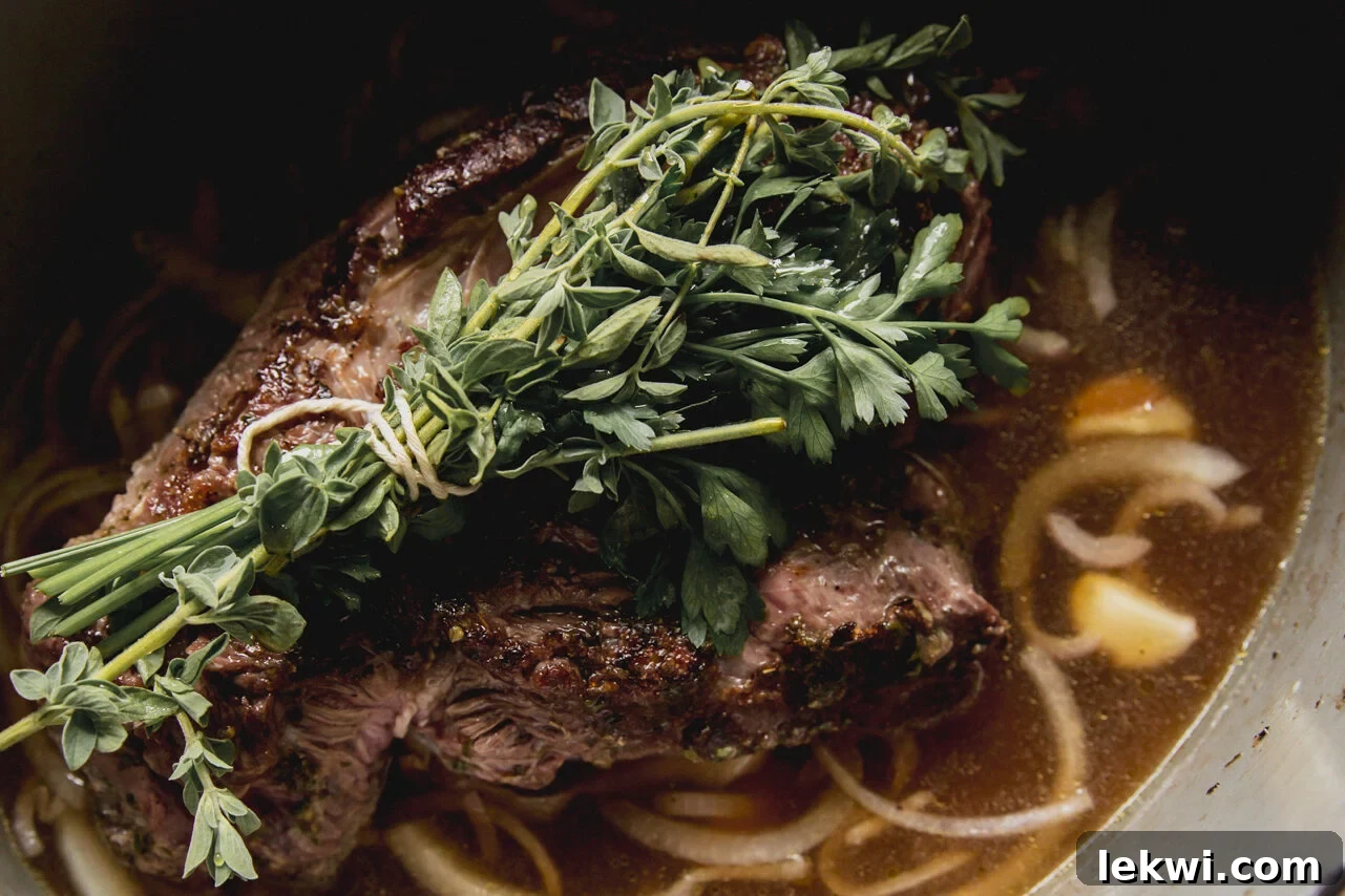 The chuck roast cooking with vinegar, onions, and an herb bundle before going into the oven.