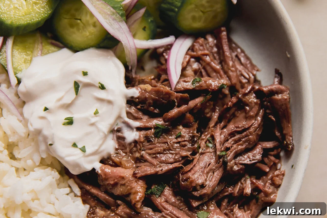 A white ceramic bowl filled with Mediterranean pot roast, served with cucumber and rice.