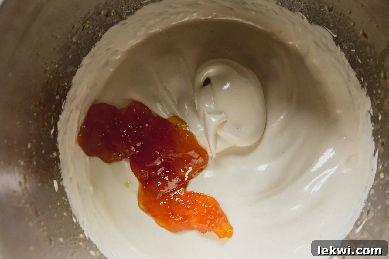 The process of folding peach jam into the whipped marshmallow fluff in a large mixing bowl.