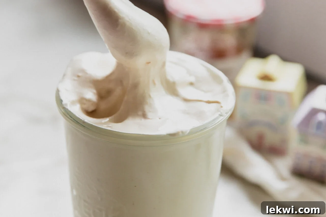 A spoon scooping the finished peach vanilla marshmallow fluff out of a clear glass storage jar.