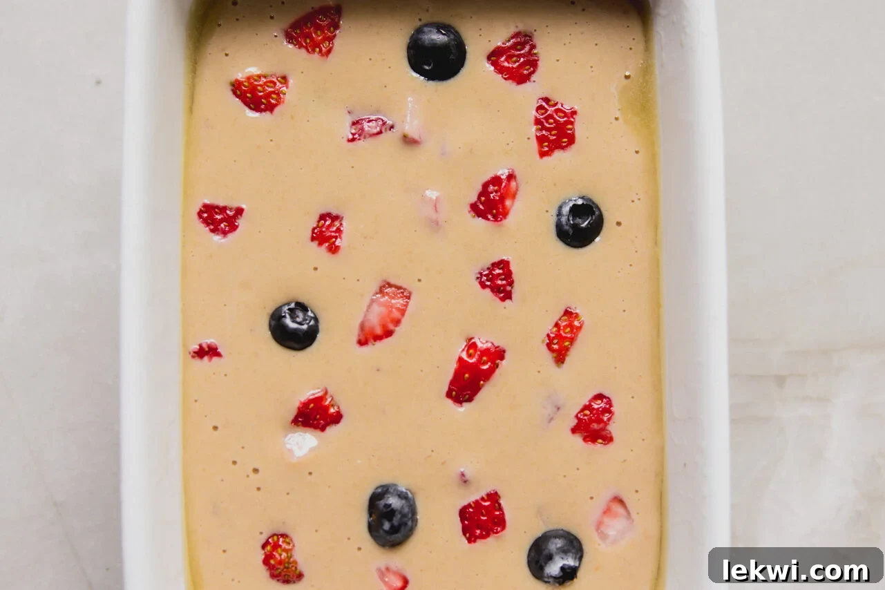 Berry Protein Breakfast Cake: High-Protein Morning Berries Bake 7 The batter for berry protein breakfast cake added to the ceramic baking dish with extra berries on top before baking.