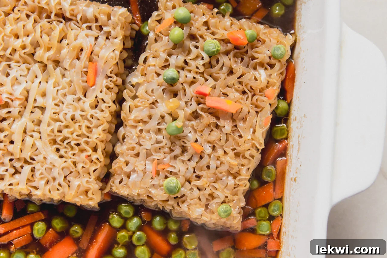 A white casserole dish with mixed vegetable and sauce topped with two ramen bricks.