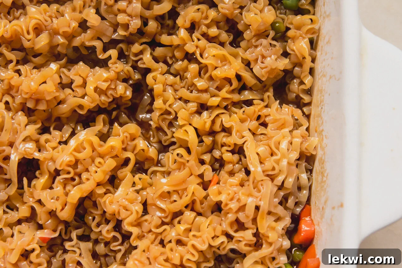 A white casserole dish with mixed vegetable, sauce, and ramen mixed in it.