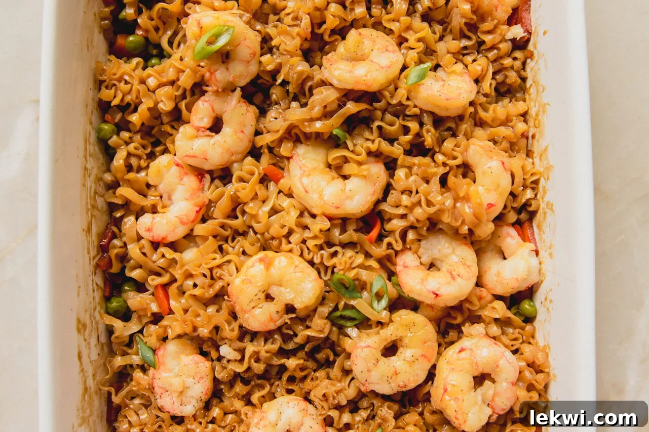 A white casserole dish with cooked shrimp on top of a ramen and vegetable sauce mixture.