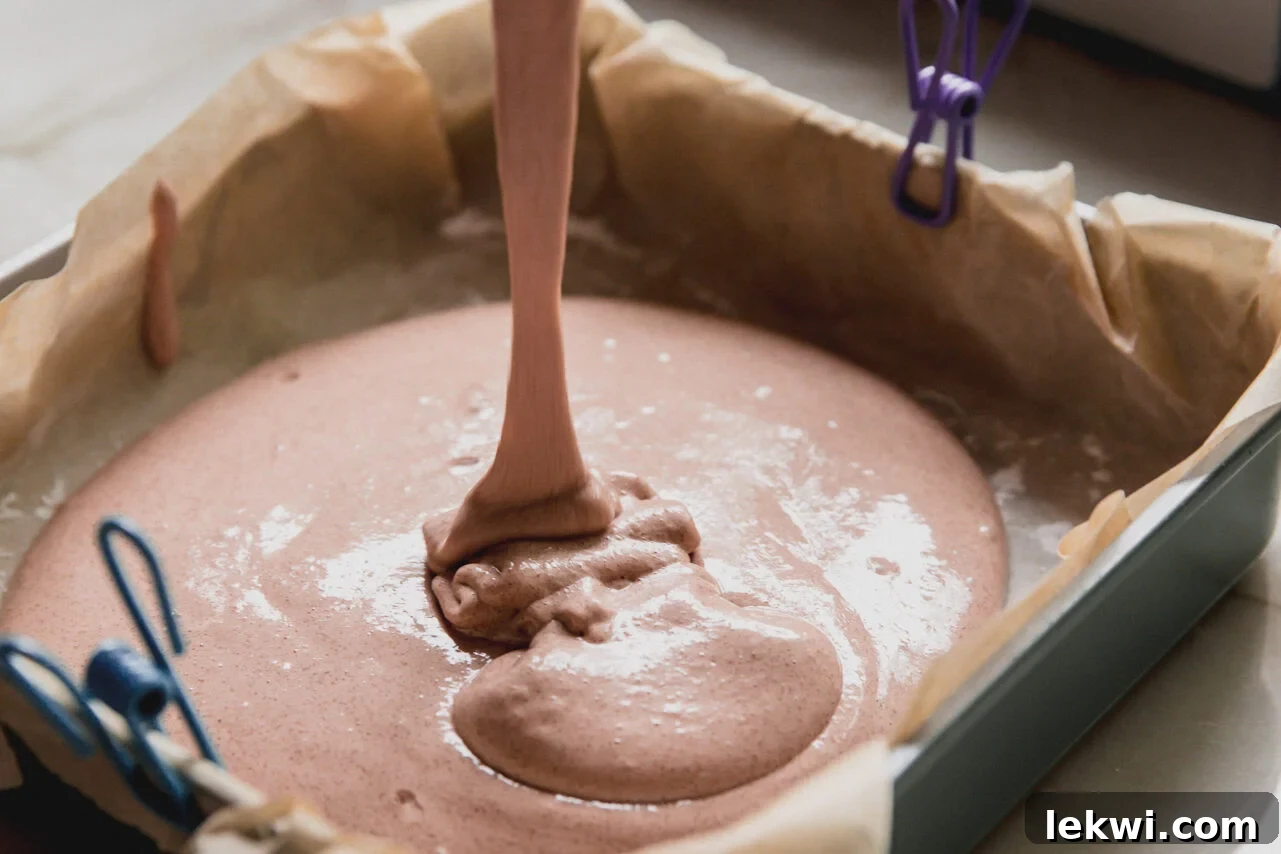 The marshmallow mixture being poured into a pan lined with parchment paper.
