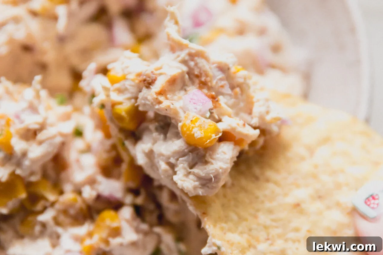 A chip taking a chunk of street corn chicken salad from the bowl.
