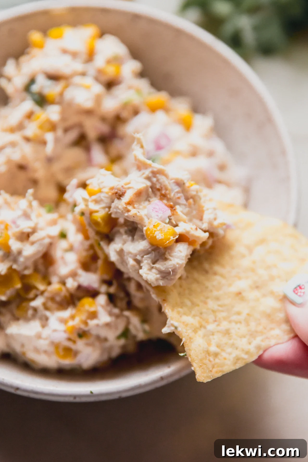 A chip taking a chunk of street corn chicken salad from the bowl.
