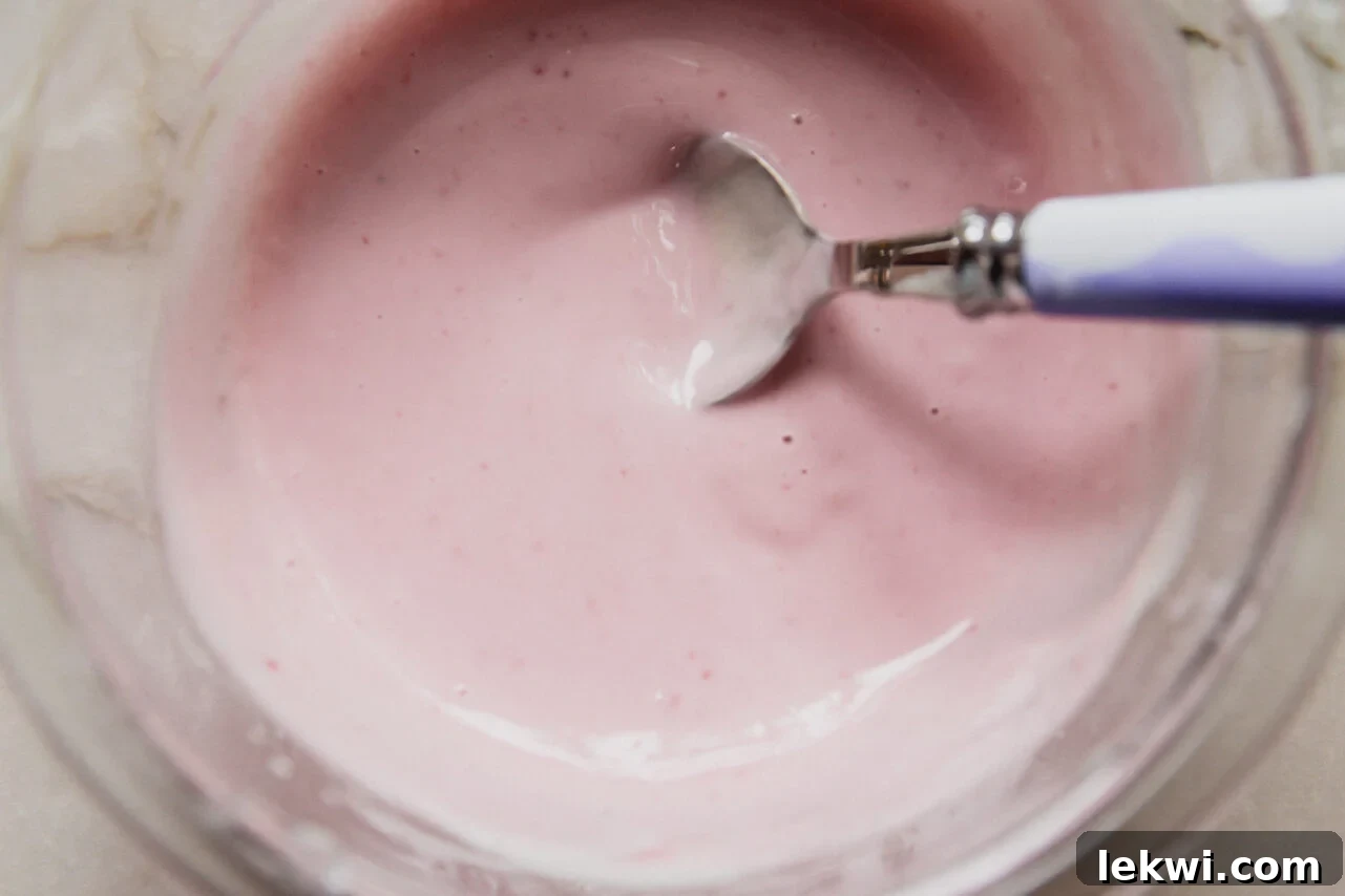 A glass bowl with a yogurt blackberry icing mixture being mixed by a spoon.
