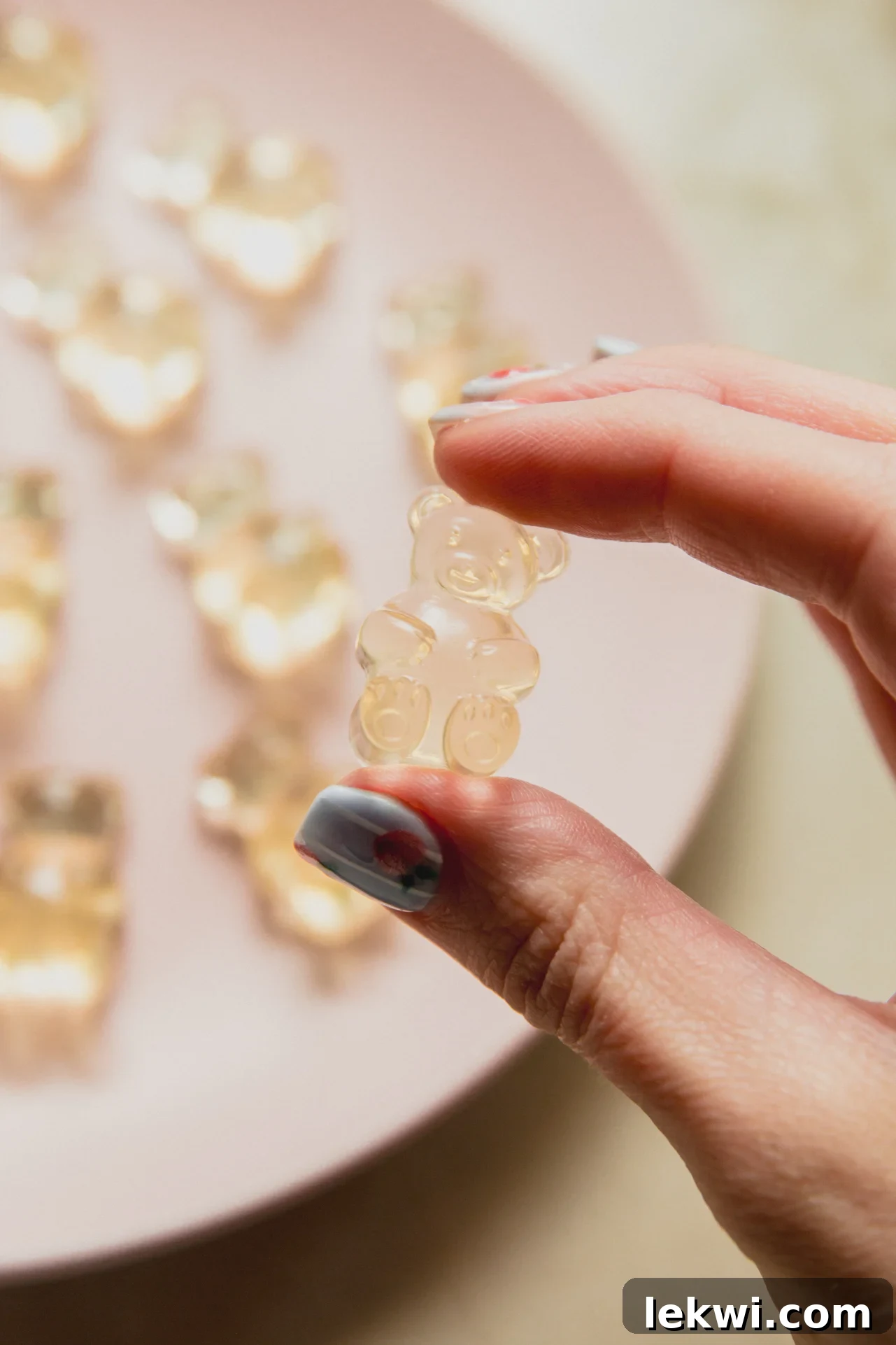 A hand holding a pickle gummy above a plate of pickle gummies.