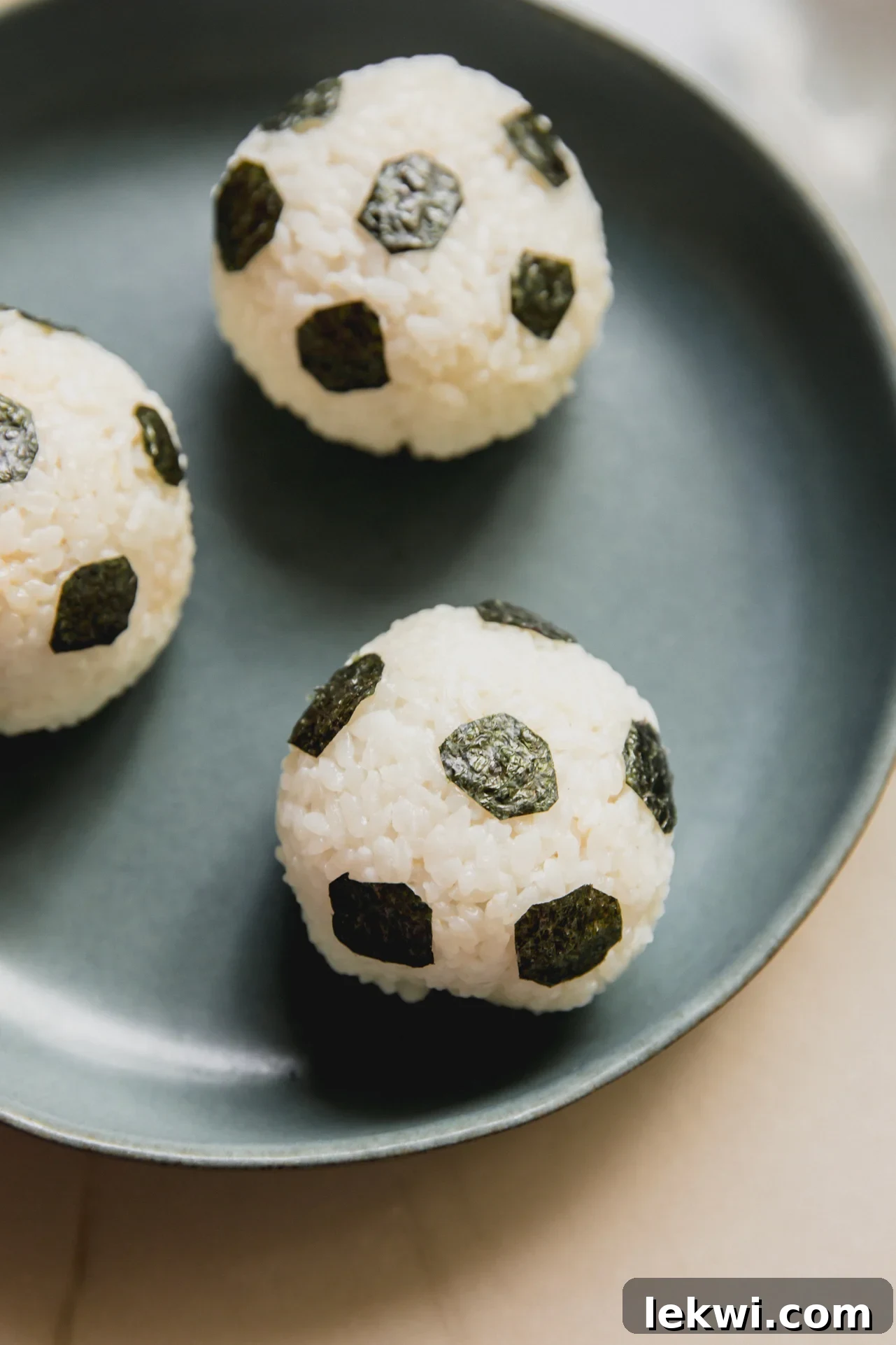 Three rice balls in a green bowl decorated with seaweed to resemble soccer balls.
