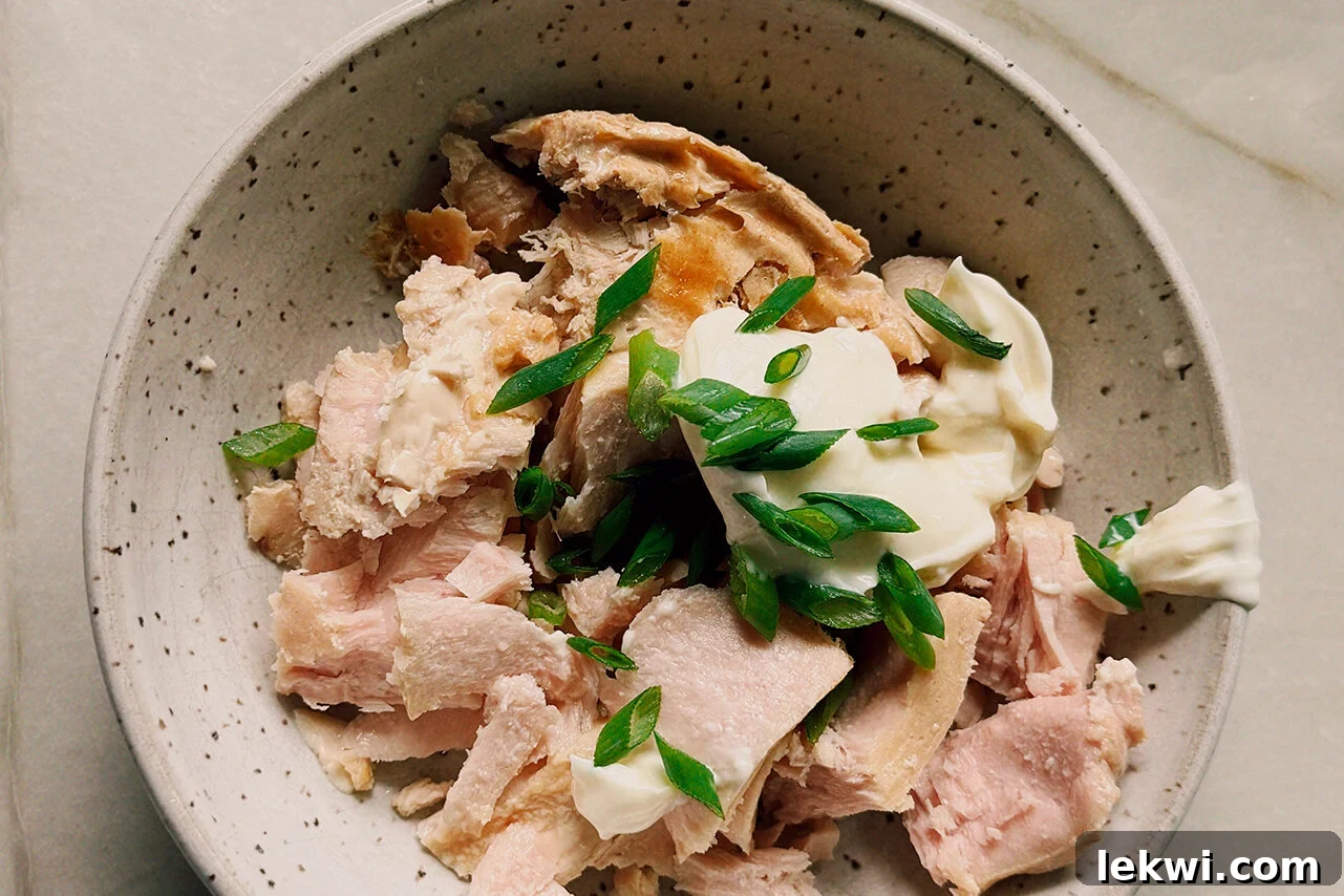A white bowl filled with tuna, mayo, and green onions before being mixed together.