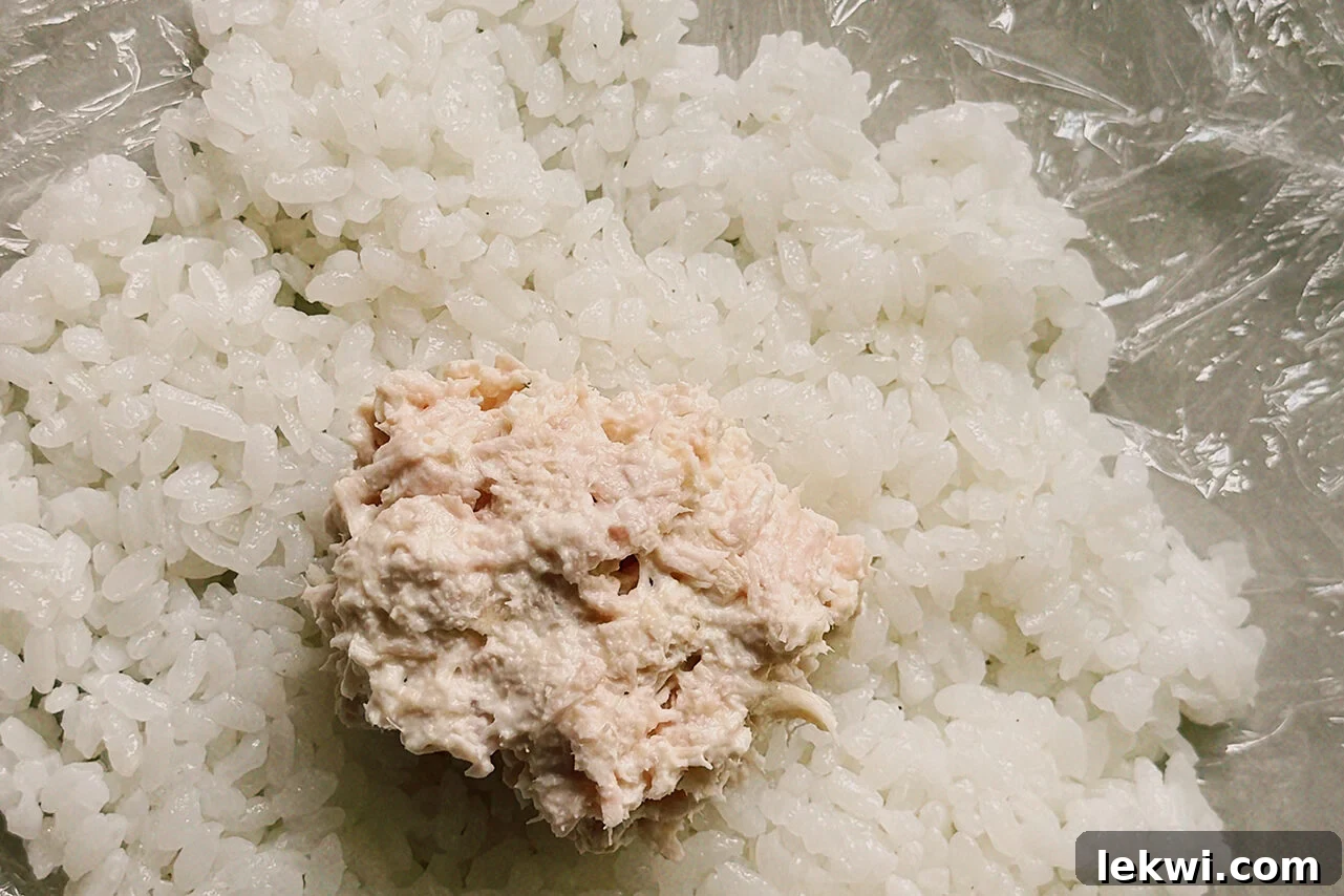 Cling wrap filed with a layer of rice and a scoop of tuna salad in the middle.