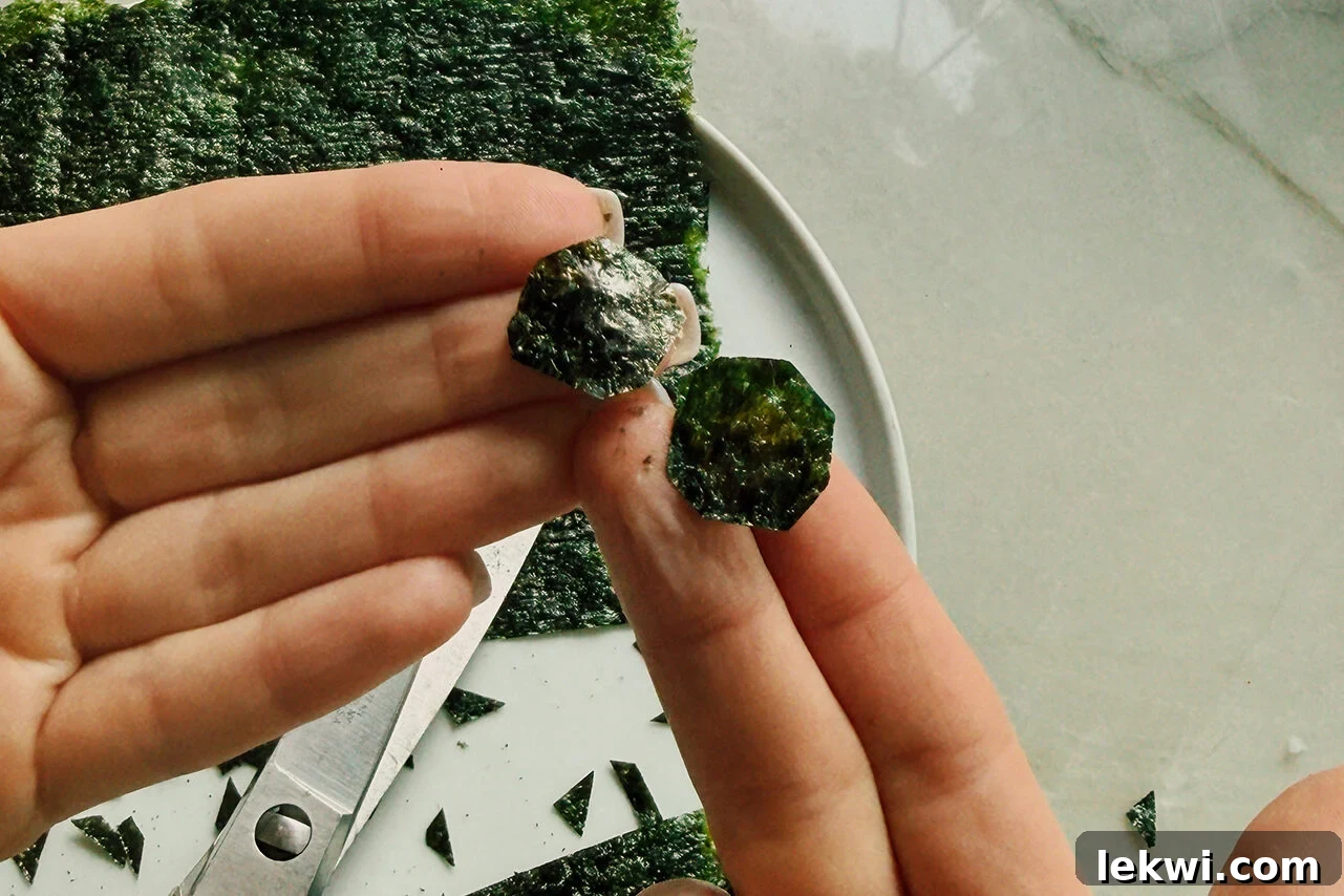 Seaweed cut into soccer balls being held in a hand above scissors and extra seaweed.