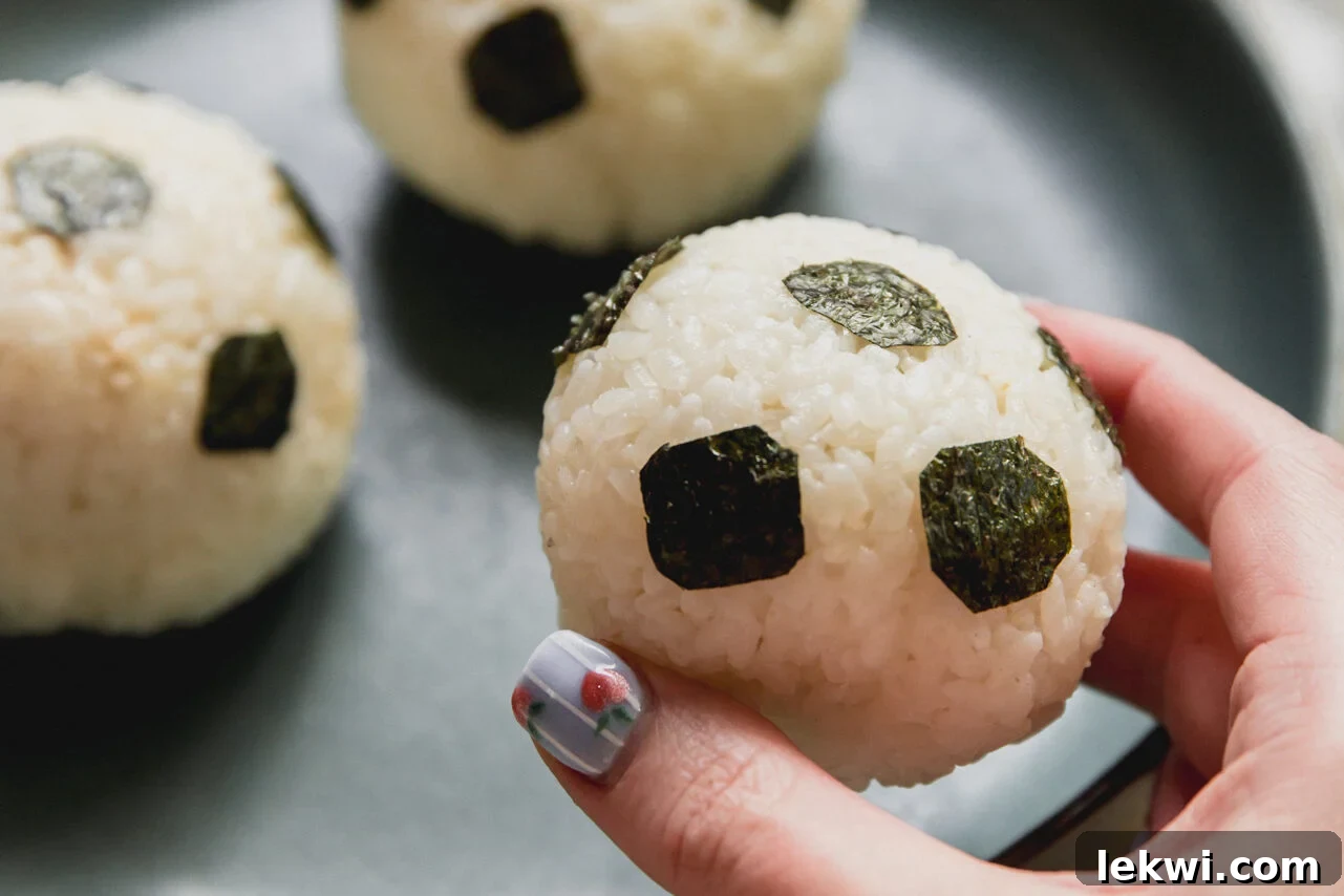 A plate with soccer tuna rice balls with a hand lifting one of the balls up.